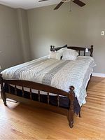 Full view of the full-size dark wood spindle bed frame with linens arranged, showing the headboard, footboard, comforter, pillows, and bed skirt.