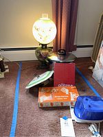 Wide view of the lot showing all items including the vintage bubble lamp lit, pot with lid, clock, chess set box, and a small blue electric device alongside an unopened box.
