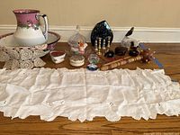 Photo showing the full lot of vintage wash basin, pitcher, cut glass dishes, brass candlesticks, pottery, and assorted collectibles arranged on wooden floor.