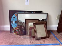 Photo showing framed wall art, decorative mask, and multiple wooden and acrylic picture frames on carpet.