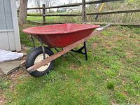 Side view of the red metal wheelbarrow showing the single rubber tire and wooden handles.