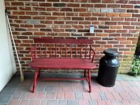 Full view of red wooden bench and black milk can next to brick wall on paved floor
