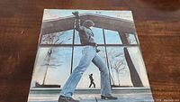 Front cover of Billy Joel Glass Houses vinyl album, showing Billy Joel standing near large glass windows.