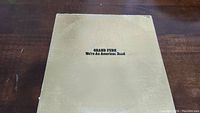 Front cover of Grand Funk Railroad vinyl album 'We're An American Band' showing beige background with black text.