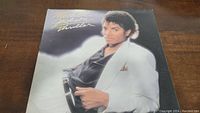Front cover of Michael Jackson Thriller vinyl album showing Michael Jackson in white suit with gold script lettering.