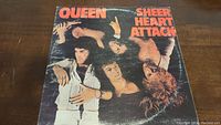 Front cover of Queen Sheer Heart Attack album showing band portrait and title in orange text on black background.