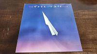 Front cover of The Parachute Club vinyl record album showing a white paper airplane on blue to purple gradient background with band name.