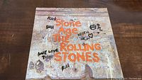Front cover of The Rolling Stones Stone Age album showing textured rock wall with orange title and handwritten band member names.