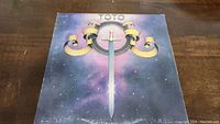 Front cover of TOTO vinyl record album showing sword and rings with space background