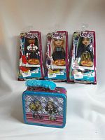 Full view of three new Bratz doll fashion packs in packaging and the Bratz lunch box with a winter-themed design showing two characters on front.