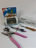 Art tool lot including Olfa mat cutter in packaging, compass, hole punch pliers with pink handles, and Försynt tracing wheel in box.
