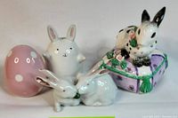 Photo showing pink egg-shaped salt and pepper shakers with white polka dots, two white bunny figurines, and the musical bunny box with floral cushion