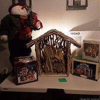 3.5' tall snowman holding gifts, wooden nativity, and three boxed porcelain houses arranged on shelf