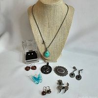 Full lot including Fossil signed necklace on display bust, multiple pairs of earrings, pendants, and brooches organized on flat surface