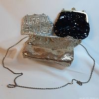 Three evening purses: gold mesh with chain strap, silver mesh with chain strap and flap, and black sequin purse with silver frame, arranged on surface.
