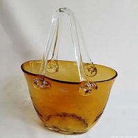 Front view of caramel colored art glass purse with clear handles on plain background.