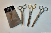 Four grooming scissors displayed on a flat surface with one pair still in the packaging.