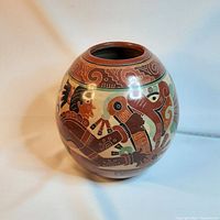 Front angle photo of the round terracotta vase featuring colorful ethnic people motifs and decorative patterns, showing vibrant painted details and smooth surface.