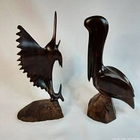 Photo showing side view of the marlin and pelican ironwood sculptures on wooden bases against plain background