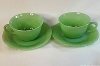 Two green jadeite cups with matching saucers showing different patterns for each saucer.