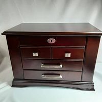 Closed wooden jewelry box with several drawers and metal handles, dark polished finish.