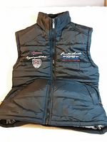 Front view of dark blue sleeveless quilted vest with visible embroidered text and flag patches on the chest area.