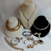 Wide view of all jewelry pieces including necklaces on stands, bracelets, earrings, brooches, and rings arranged on a white background.