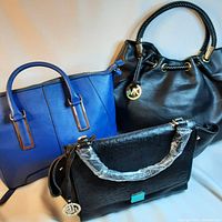 Three handbags: black Michael Kors bag with braided handles, blue structured handbag, black textured handbag with turquoise accent and wrapped handles.