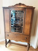 Front view of antique wooden hutch cabinet, showcasing decorative wood details, glass door with wood muntin design, and single drawer with metal handles.