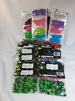 Various packages of mini pompoms in multiple colors including purple, red, green, pink, and blue in sealed plastic bags.