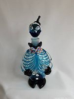 Full view of the clown-shaped Murano glass decanter, showing blue and white swirled body, black feet and hands, and colorful bow tie.
