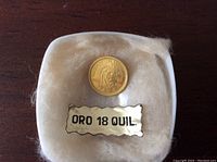 Coin obverse showing Cacique Tamanaco portrait and packaging label "ORO 18 QUIL." in foam-padded plastic case