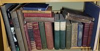 Books arranged tightly on a shelf showing mostly hardcover volumes with varied colors and visible aging, including damaged spines and frayed covers.