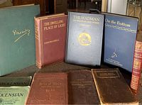 Eight antique books arranged in two rows on a table showing various colored hardcovers and titles.