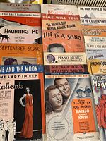 Photo showing multiple vintage sheet music covers with titles like 'Haunting Me,' 'September Song,' and 'The Magic Pianist' among others, with various illustrated and photographic covers.