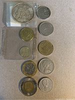 Top view of all coins laid out showing the 1966 Hercules silver coin in protective casing and an assortment of foreign coins.