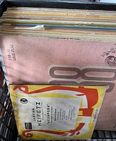 Photo showing a box filled with tightly packed vintage 78 RPM vinyl records in original covers; foreground features Jascha Heifetz album cover with prominent red and yellow graphics.