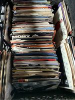 Over 200 45 RPM vinyl records in original cardboard sleeves stacked vertically in a crate.