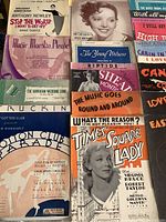 Photo showing a selection of vintage musical score sheets with titles and artwork, including 'Stop the World I Want to Get Off,' 'The Young Virtuoso,' and 'The Hawaiian Wedding Song.'