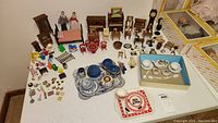 Full overview of various antique and vintage dollhouse furniture and miniature tea sets arranged on a table.