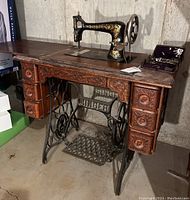 Full view of Singer sewing machine installed in carved wood cabinet on cast iron treadle base