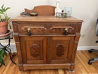 Front view of antique wooden cabinet showing drawer, double doors with brass and black handles.