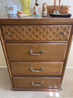 Front view of the Bassett wooden dresser showing four drawers including one with lattice design, silver pull handles, and various decorative items on top.