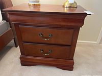 Front view of wooden bedside table with two drawers and brass handles, showing overall condition and style.