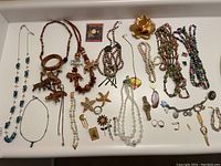 Photo showing a variety of costume jewelry, 2 rings marked 10k gold, multiple beaded necklaces, wooden bangles and several pins including flower and starfish shapes.