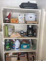 Photo showing shelving unit filled with the crockpot, coffee maker, kitchen appliances, accessories, and towels.