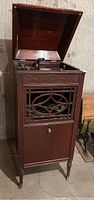 Front view of the Edison phonograph with lid open showing the disc player and part of the horn, housed in wooden cabinet with lattice front panel.