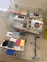 Top view of clear plastic storage box containing sewing notions such as black buttons, needles, thread spools, and fabric patches.