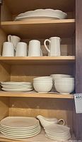 Three shelves in cabinet showing mugs, bowls, plates, and large platters.