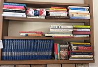 Wide view of multiple books on wooden shelves including genealogy books and biographies